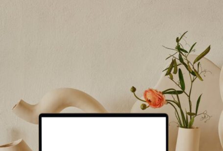 Surface Laptop - Netbook with white screen placed on shelf near uneven curved ceramic vases with flowers with green leaves near pipes in light room with white wall