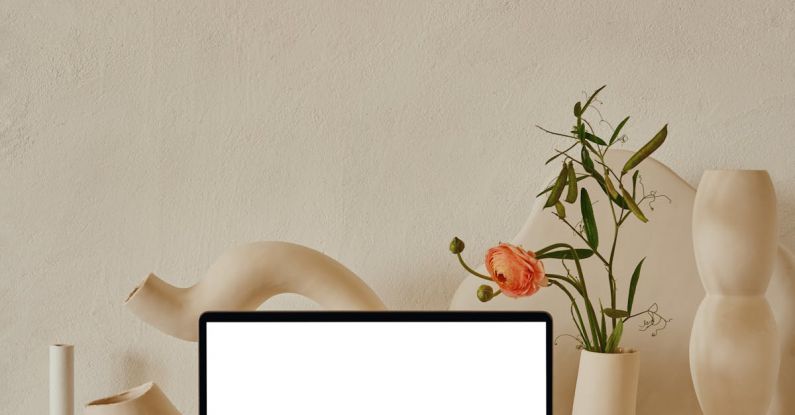 Surface Laptop - Netbook with white screen placed on shelf near uneven curved ceramic vases with flowers with green leaves near pipes in light room with white wall