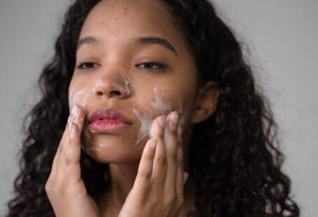 Girl, Wash Your Face - African American female with long dark curly hair washing cheeks with facial foam on gray background