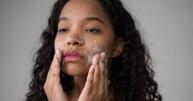 Girl, Wash Your Face - African American female with long dark curly hair washing cheeks with facial foam on gray background