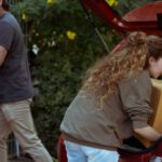 Get Out - Young woman with curly hair getting carton box out from trunk of automobile while cheerful ethnic man carrying box into new home in suburb or countryside area