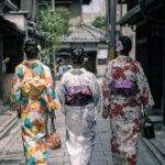 Kimono - Three Geisha Walking Between Buildings